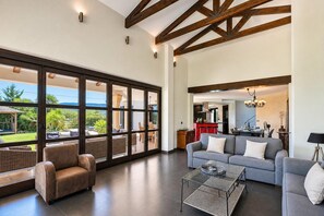 Un vaste espace de vie avec une grande porte vitrée donnant sur un patio extérieur, un canapé gris, un fauteuil en cuir marron et une table basse en verre.