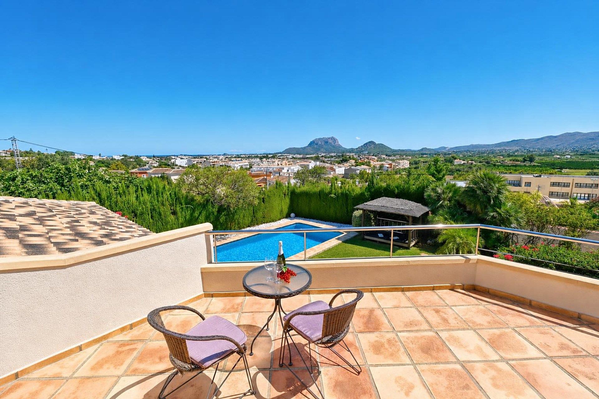 A rooftop terrace with a pool, two wicker chairs, and a table with a bottle and glass.