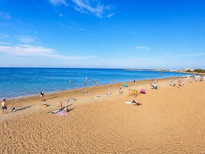 A beach with people sunbathing and swimming, a clear sky, and a calm sea.