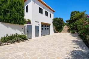 A two-story building with a white facade, a tiled roof, and a stone-paved driveway leading to a garage.
