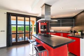 A modern kitchen with a central island, black countertops, and red cabinetry.