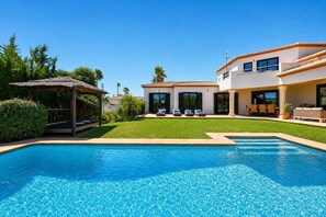 A swimming pool with a clear blue surface, surrounded by a well-maintained lawn and a building with a tiled roof.