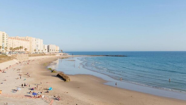 Una playa con arena, algunas personas y edificios al fondo.