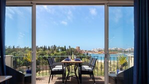 Ein Balkon mit Tisch und Stühlen, Blick auf das Meer und eine Stadtlandschaft im Hintergrund.