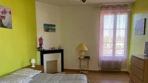 Ein Schlafzimmer mit Bett, Nachttisch, Lampe, Kommode, Kamin und einem Fenster mit Vorhängen.