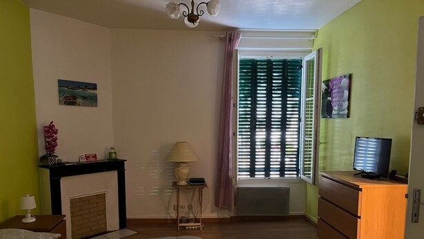 Ein Schlafzimmer mit Bett, Kommode, Lampe, Kamin und einem Fenster mit Jalousien.