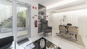 A modern hotel lobby with a glass door entrance, a seating area with a black leather couch, a dining table with chairs, and a large wall mural. - FAA Rentals 31 de Janeiro 3A,the city at your feet (Funchal)