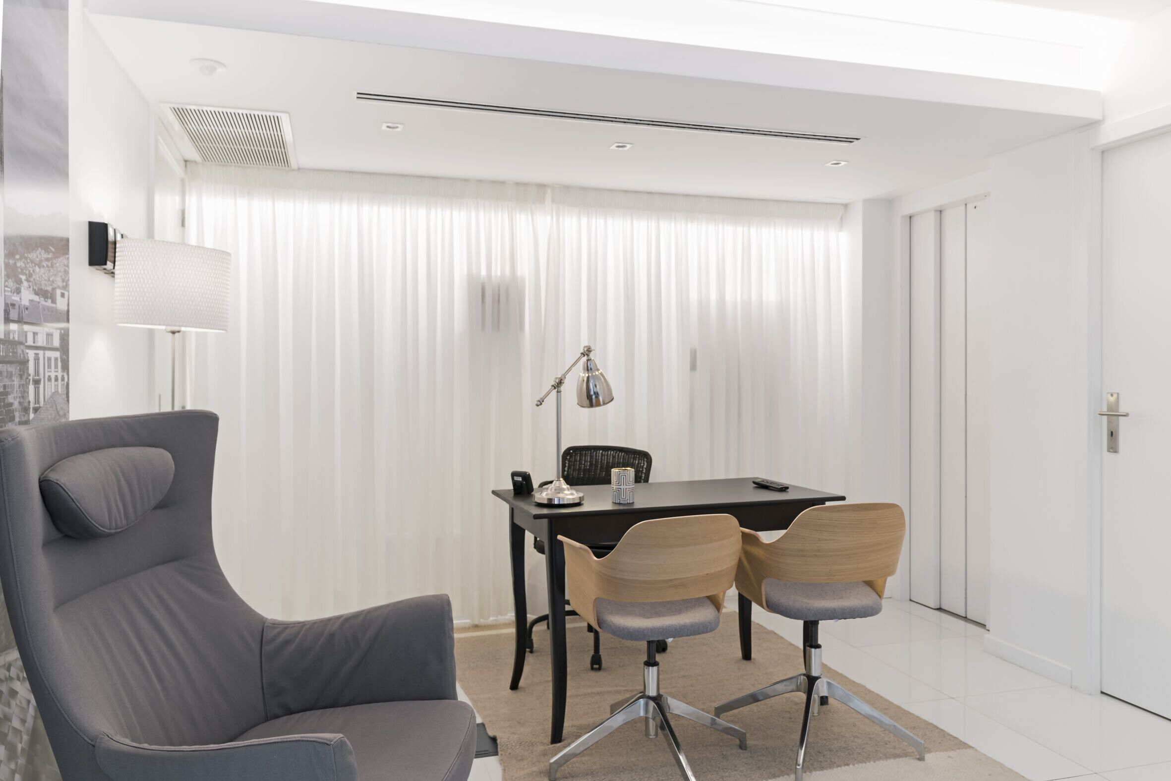 Une pièce moderne avec un canapé gris, un bureau noir et deux chaises.