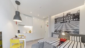 A modern hotel room with a dining area, two beds with striped bedding, a gray sofa, and a large wall mural. - FAA Rentals 31 de Janeiro 3A,the city at your feet (Funchal)