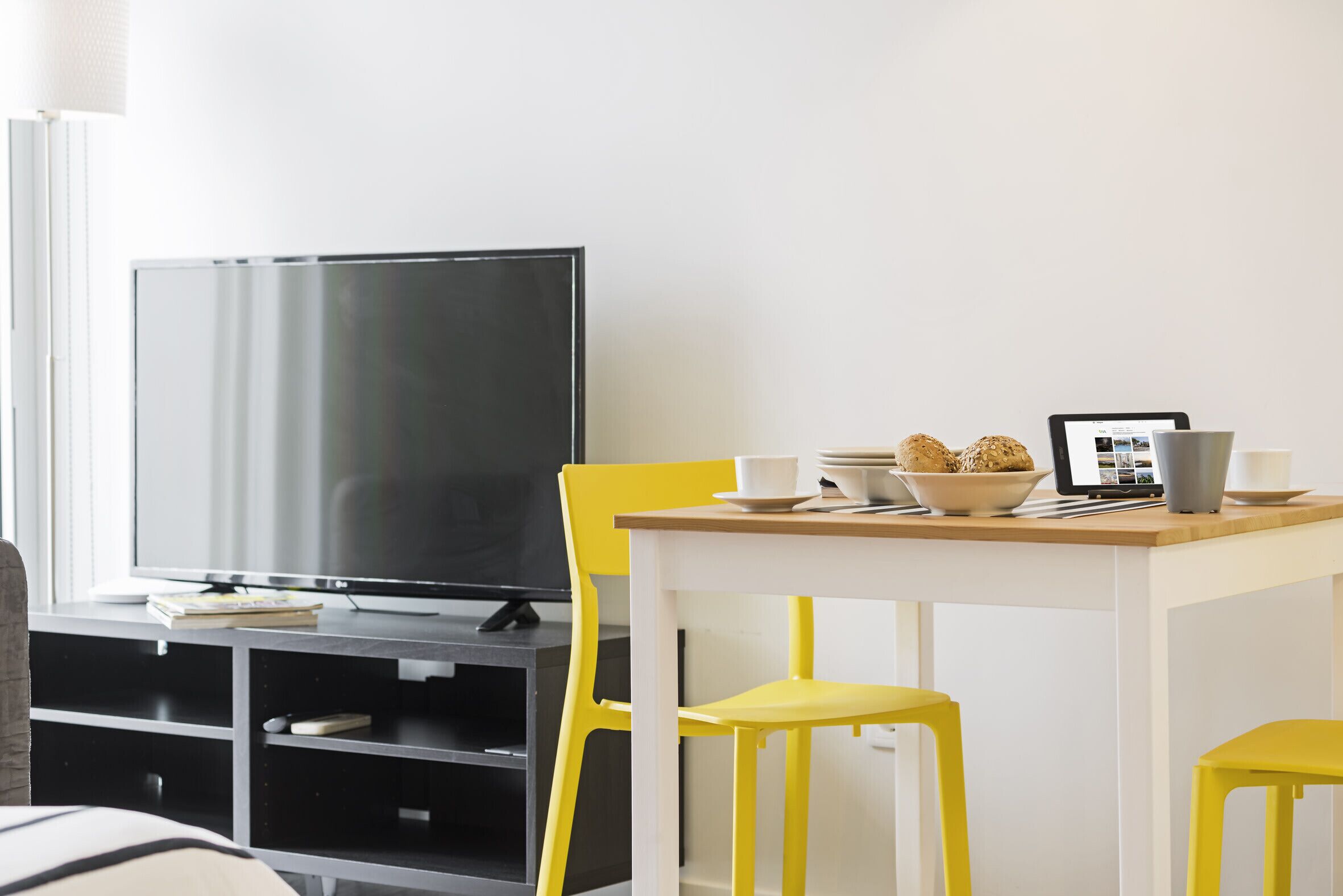 Un salon moderne avec un téléviseur à écran plat, des fauteuils jaunes, une table en bois et un bol de biscuits.