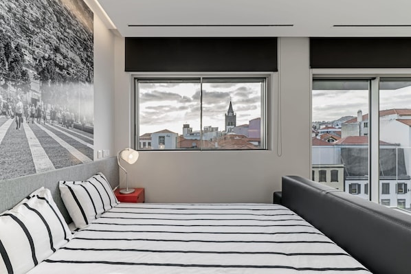 Una moderna camera d'albergo con un grande letto, vista sulla città attraverso una finestra e un murale sulla parete.
