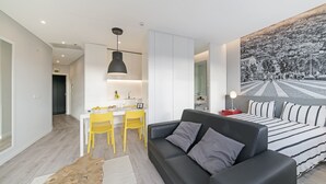 A modern living room with a black leather sofa, a wooden coffee table, and a dining area with yellow chairs.