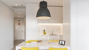 A modern kitchen with white cabinets, a black pendant light, and a dining table with yellow chairs.