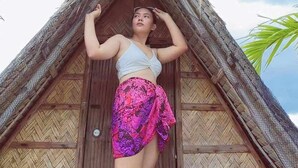Una persona de pie frente a una cabaña con techo de paja y puerta de madera.