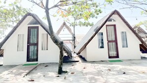 Dos pequeñas casas de campo blancas, con techos triangulares, puertas y ventanas de madera oscura, rodeadas de árboles y un cielo despejado.