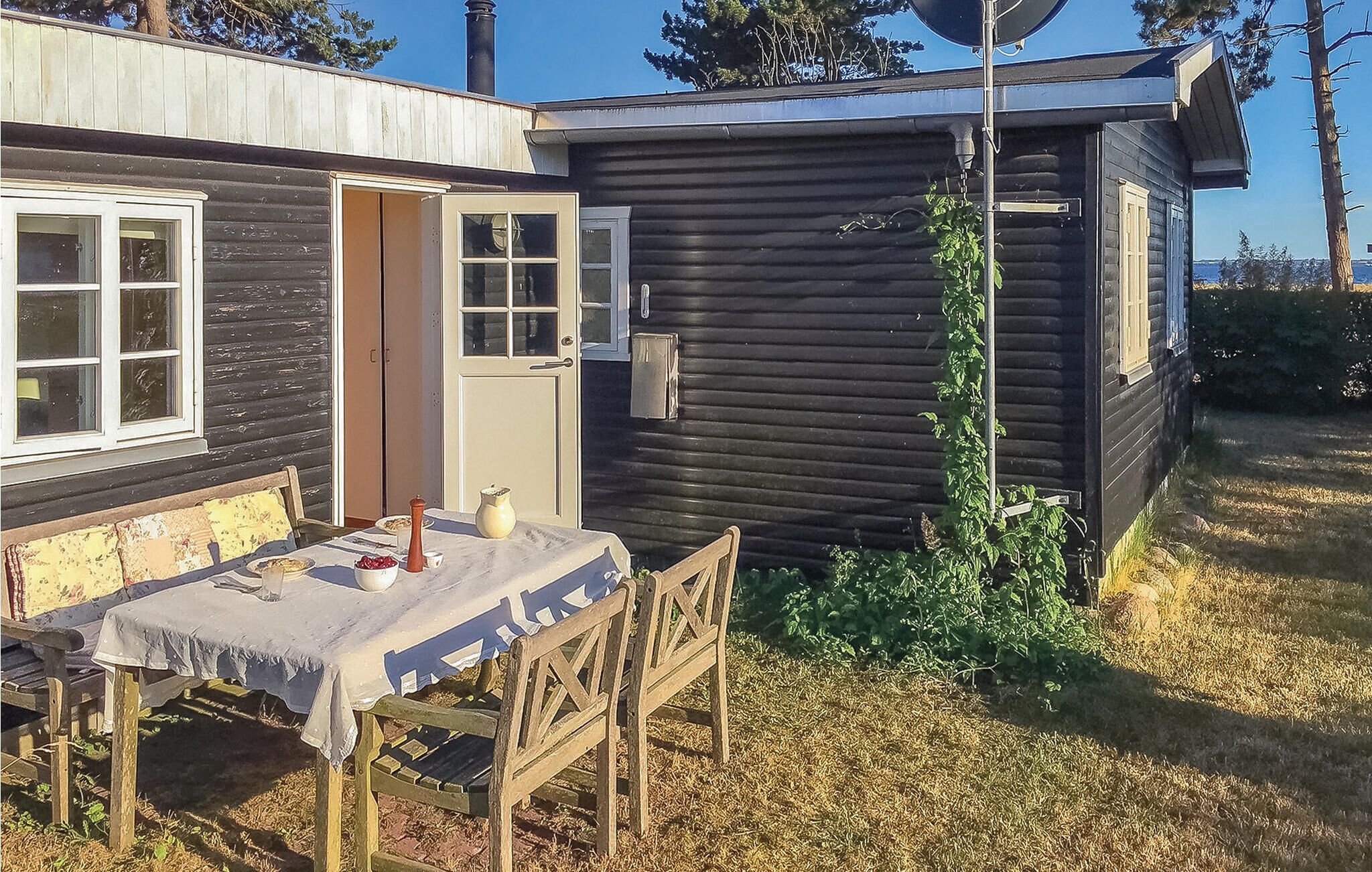 A wooden cabin with a dining table set outside, a door, and a small garden area.