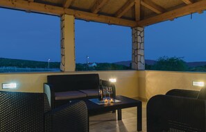 Relax in this serene outdoor seating area with a stone pillar and a wooden ceiling, featuring two comfortable chairs and a small table.
