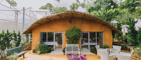A rustic building with a thatched roof, large windows, and a patio area with outdoor furniture.