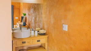 Un baño con tocador de madera, un lavabo redondo, un espejo y un perchero para toallas.