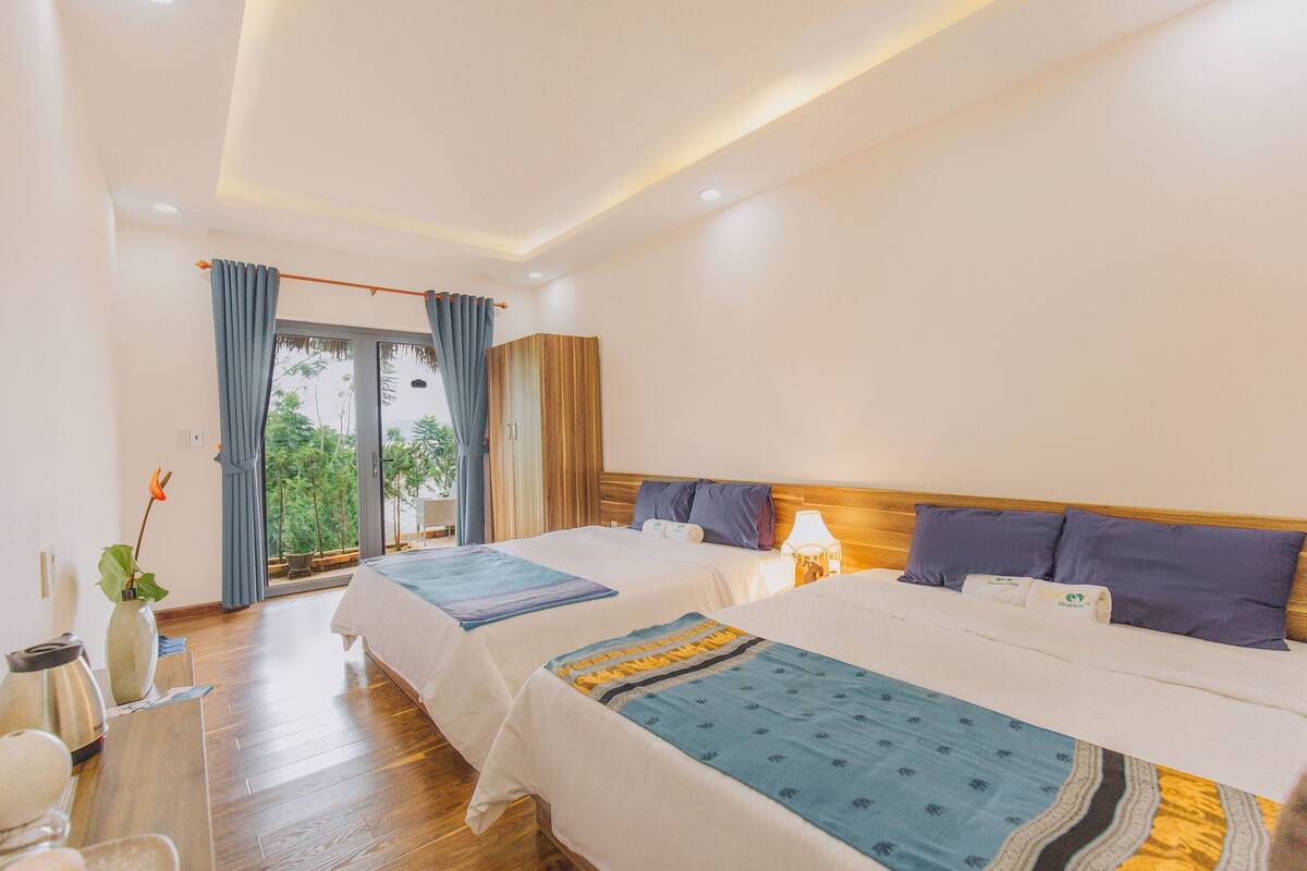Habitación de hotel con dos camas, piso de madera, un ventanal grande con cortinas y vistas a zonas verdes.
