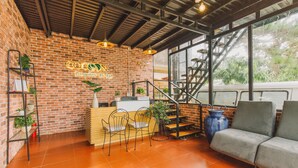 Un área de recepción con pared de ladrillo, mostrador de madera, sillas metálicas y una escalera que sube a un nivel superior.
