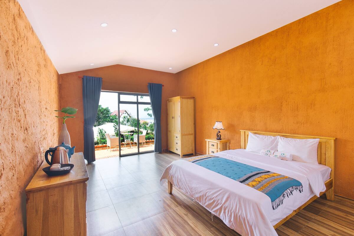 Habitación de hotel con una cama grande, mesitas de noche de madera, un armario y vistas al exterior a través de una puerta de vidrio.