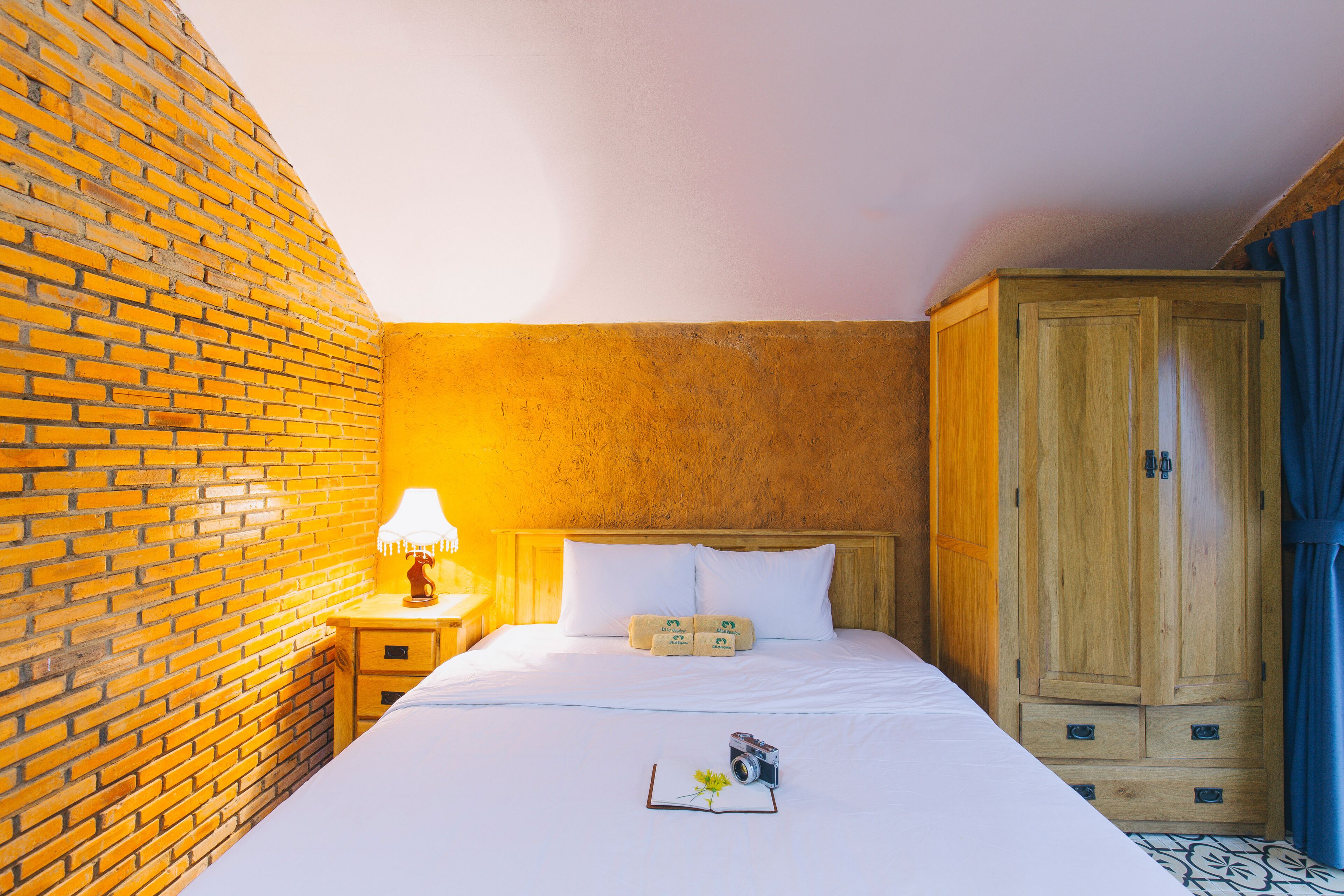 Ein Hotelzimmer mit Ziegelwand, Holzschrank, Bett mit weißer Bettwäsche und Nachttisch mit Lampe.