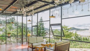 Un balcón amplio con sofá, sillas y mesa, con vistas a un jardín exuberante y montañas lejanas.