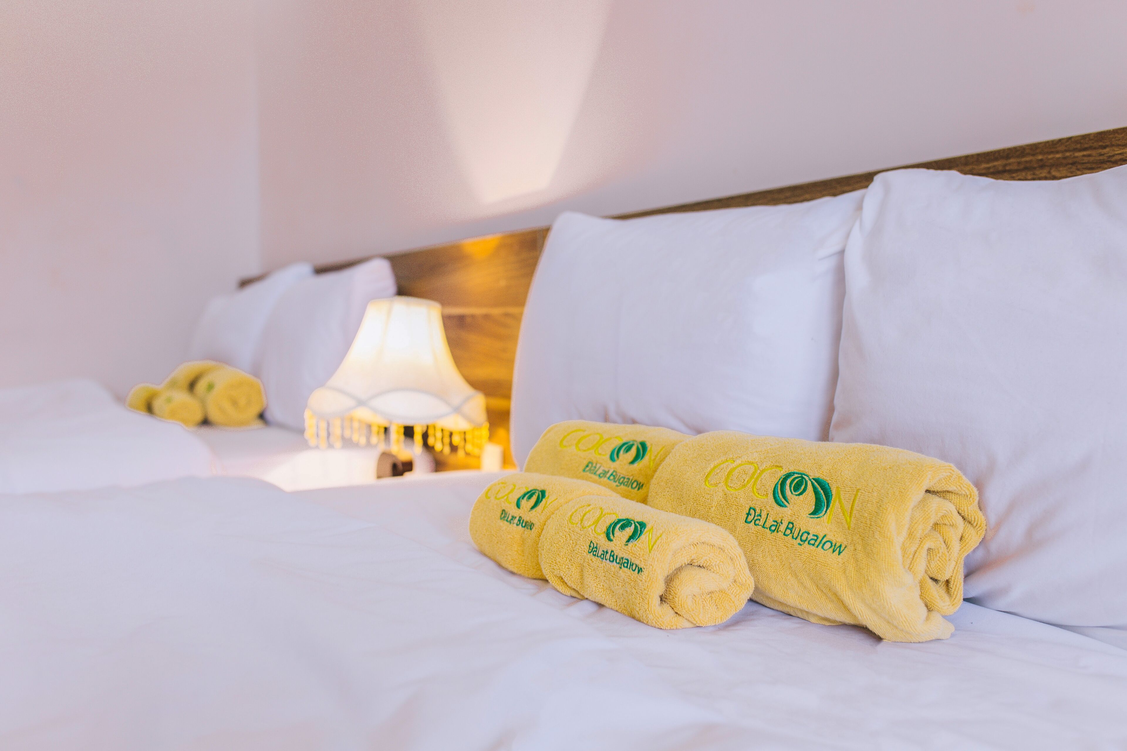 A hotel room with neatly made beds, white linens, and rolled towels with a logo.