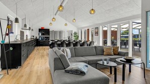 Eine moderne Küche mit einer zentralen Kochinsel, einem Essbereich mit großem Tisch und einem Wohnbereich mit Sofa und Couchtisch.
