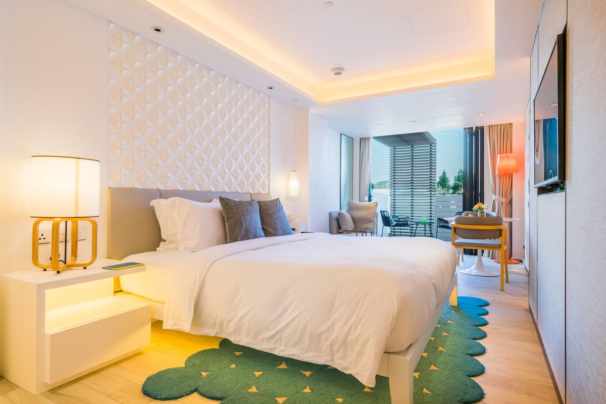 Une chambre d’hôtel moderne avec un grand lit, des tables de chevet, un bureau et une vue sur l’extérieur.