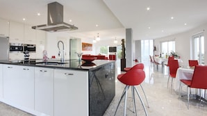 A modern kitchen with white cabinets, a central island, and red chairs in the dining area.
