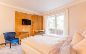 Quarto de hotel com uma cama, escrivaninha, poltrona, televisão e varanda com vista.