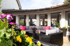 Un espacio de estar al aire libre cubierto con un sofá, muebles de mimbre y plantas en macetas.