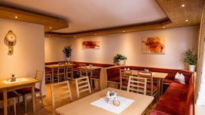 A restaurant with wooden tables and red cushioned booths, a wall clock, and abstract paintings. - Top 1 - House Annette (Schröcken)