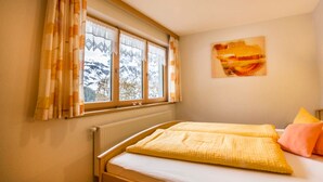 A bedroom with a bed, a window with curtains, a radiator, and a painting on the wall. - Top 1 - House Annette (Schröcken)