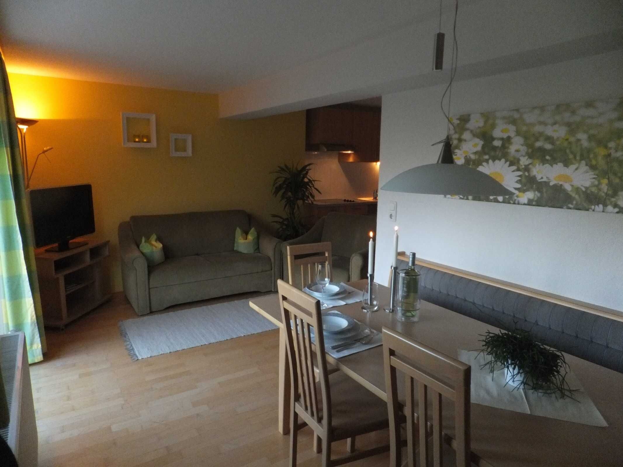 Un salon comprenant un canapé, un téléviseur, une table à manger avec des chaises et une plante.