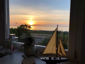 A room with a large window overlooking a sunset, a small sailboat model, and a plush toy on a windowsill. - Fritzi, Glowe on Rügen, Germany (Glowe)