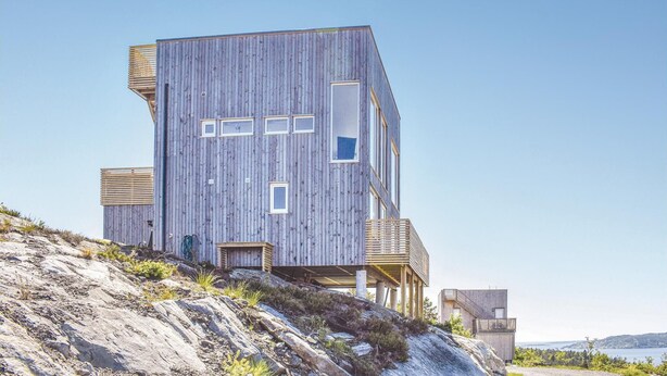 Un bâtiment moderne en bois, à plusieurs niveaux et doté de grandes fenêtres, situé sur une colline rocheuse et offrant une vue dégagée sur le paysage environnant.
