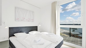 Une chambre d’hôtel avec un grand lit, une tête de lit, une vue sur la mer et un tableau au mur.