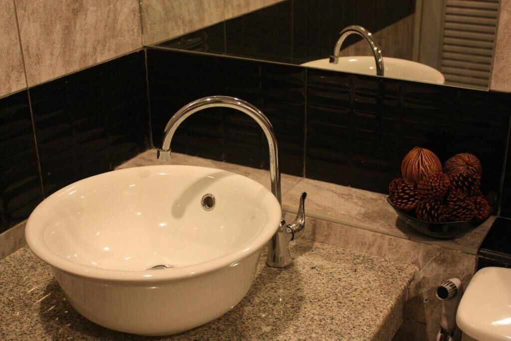 A bathroom with a white sink, a mirror, and a bowl of pine cones on the countertop.