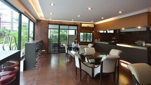 A modern restaurant with a long counter, multiple seating options, and large windows offering a view of the outdoors. - LOFT Salaya (Phutthamonthon)