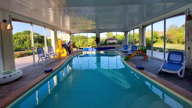 An indoor swimming pool with clear glass walls, blue lounge chairs, and a slide.