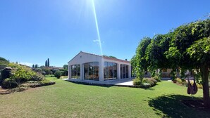 A modern house with a large glass extension, surrounded by a well-maintained lawn and a variety of trees.