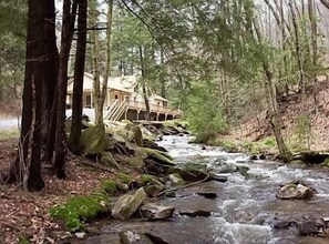 Escape to a serene riverside retreat with a cozy cabin-style building surrounded by tall trees and a gentle river.