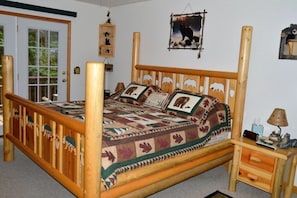 Uma cama de madeira com roupa de cama com tema de animais, uma mesa de cabeceira com abajur e um painel de parede com tema de urso.