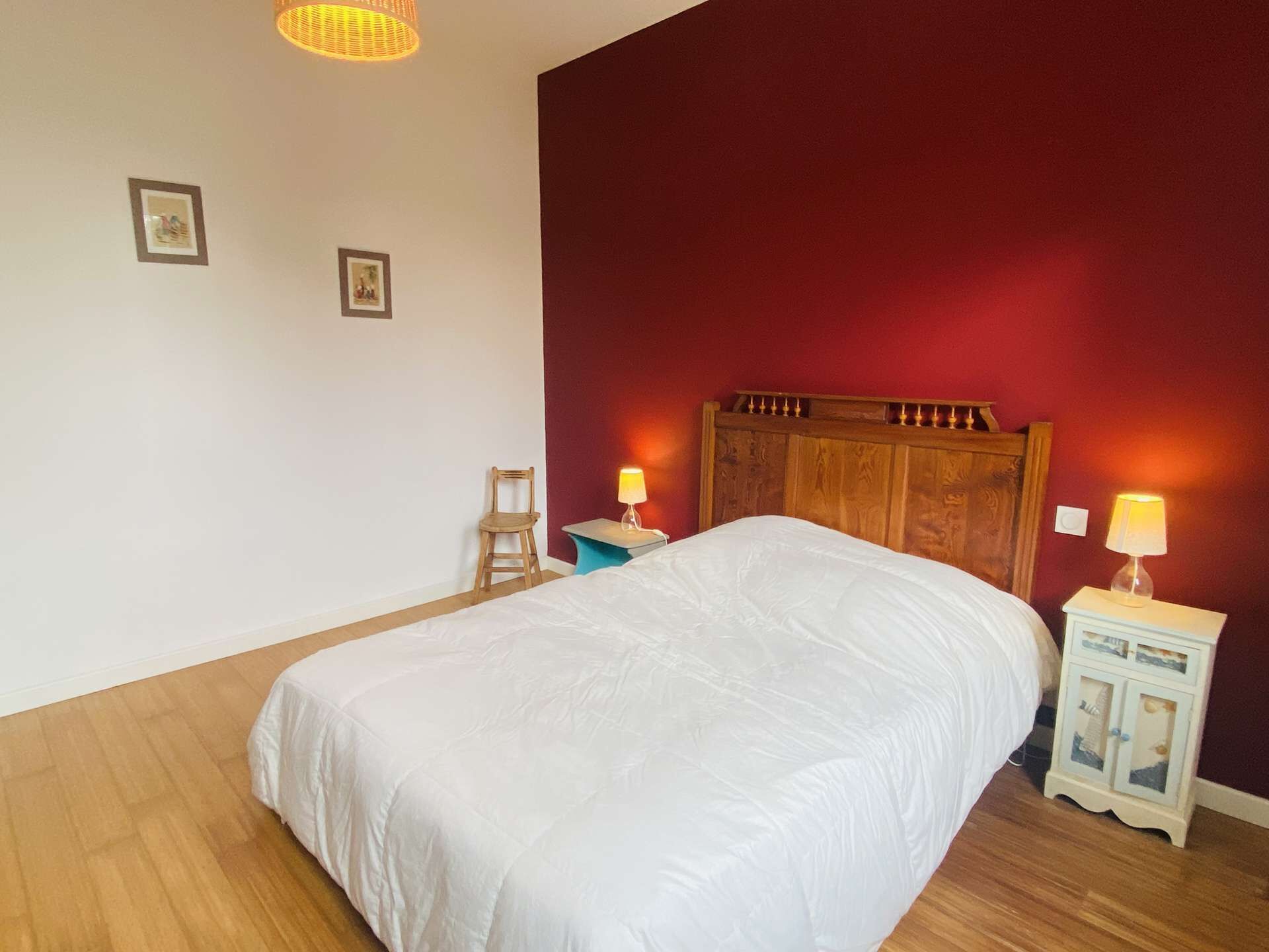 A bedroom with a wooden bed, two bedside tables with lamps, a chair, and two framed pictures on the wall.