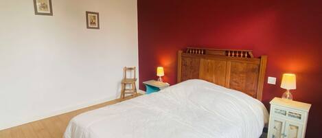 A bedroom with a wooden bed, two bedside tables with lamps, a chair, and two framed pictures on the wall.