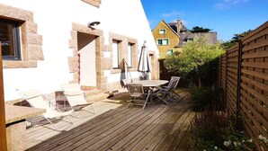 A wooden deck with a round table and chairs, a small outdoor seating area with a table and chairs, and a wooden fence. - La Baïta spacious house 200m from the beach (Trégastel)