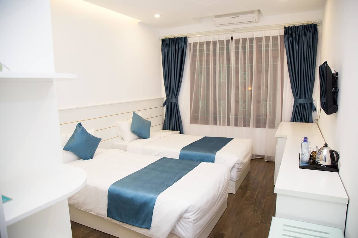 Quarto de hotel com duas camas, uma mesa, uma cadeira, televisão e janela com cortinas.